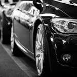 Close-up black and white image of a luxury car line-up focusing on vehicle headlights.