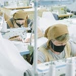 Workers engaged in sewing operations at a busy textile manufacturing factory.
